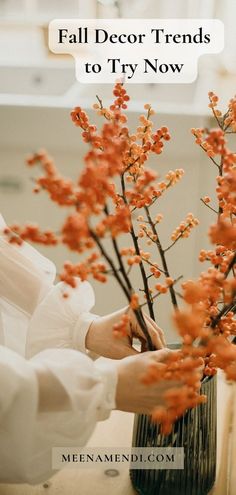 a woman arranging flowers in a vase with text overlay that reads fall decor trends to try now