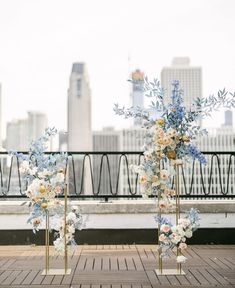 two tall vases with flowers are sitting on the ground in front of a cityscape