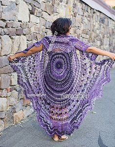 a woman is walking down the street wearing a purple crocheted shawl