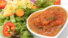 a white bowl filled with sauce next to a salad on top of a white plate