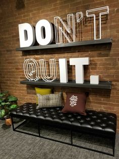 a black bench sitting in front of a brick wall with don't quit out letters on it