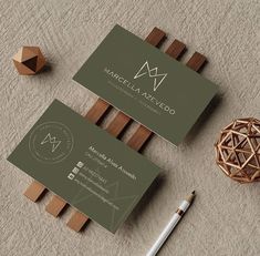 two business cards sitting on top of a table next to a pen and wooden object