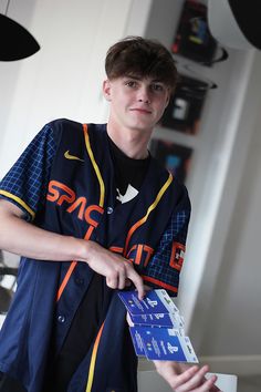 a young man in a baseball uniform is holding a card and looking at the camera