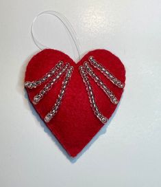 a red heart shaped ornament with chains hanging from it's side on a white surface