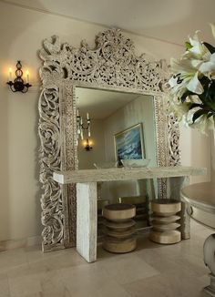 an ornate white mirror sitting on top of a table next to a vase filled with flowers