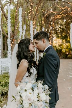 a bride and groom standing in front of an outdoor ceremony arch with white flowers on it