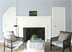 two chairs and a table in front of a fireplace with blue paint on the walls