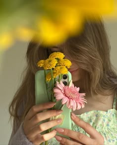 a woman is holding flowers and taking a selfie with her cell phone in front of her face