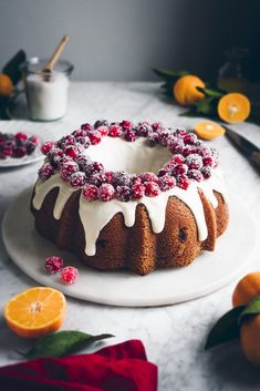 a bundt cake with white icing and cranberries on top, surrounded by oranges