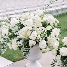 two white vases filled with flowers sitting on top of a cement slab in front of rows of chairs