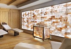 a room with wooden floors and white chairs in front of a large wall made out of stones