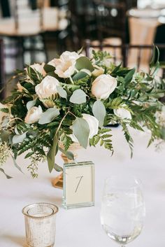 a vase with white flowers and greenery on a table