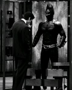 two men in suits are standing next to a batman statue