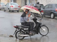 a man on a motor scooter holding an umbrella in the rain with cars behind him