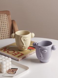 two mugs sitting on top of a table next to a book and other items