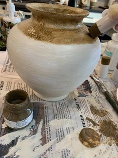 a large white vase sitting on top of a table next to paint and other items