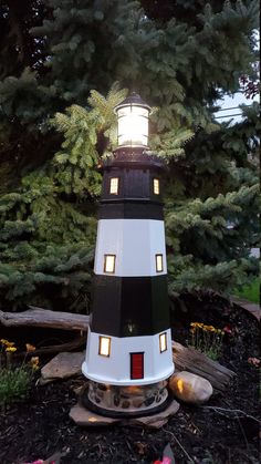 a black and white lighthouse sitting on top of a pile of dirt next to trees