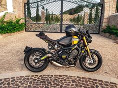 a black and yellow motorcycle parked in front of a gated entrance to a house