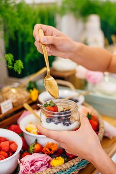 a person holding a spoon full of yogurt with berries and strawberries in bowls