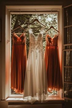 three bridesmaid dresses hanging on a window sill