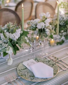 the table is set with white flowers and greenery, candles and napkins on it