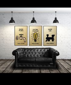 a black leather couch sitting in front of two framed posters on a wall next to a brick wall