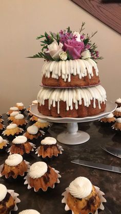 a table topped with lots of cupcakes covered in frosting next to a cake