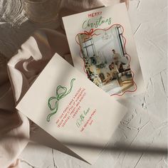 two christmas cards sitting next to each other on top of a white tablecloth covered floor