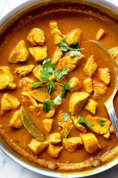 a pan filled with chicken curry and garnished with cilantro on the side