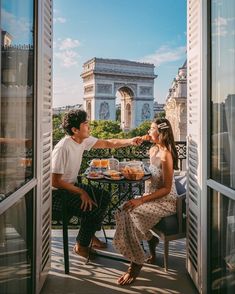 a man and woman sitting at an outdoor table with food in front of the eiffel tower