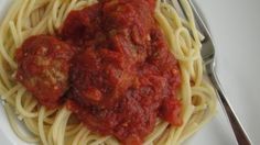 spaghetti with meatballs and tomato sauce on a white plate next to a silver fork