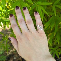 a woman's hand with a ring on it and green plants in the background