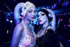 two women dressed up in costumes pose for a photo at a costume party with lights behind them