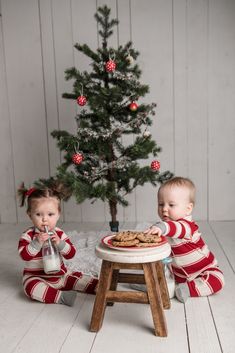 two babies sitting in front of a christmas tree eating cookies and drinking milk from bottles