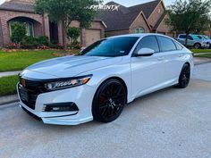 a white car is parked in front of a house with black wheels and rims