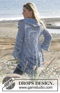 a woman is walking on the beach wearing a crocheted shawl and boots