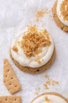 three cookies with white frosting and crumbs on top, next to crackers