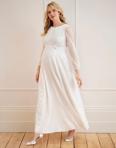 a woman in a white dress standing on a wooden floor with her hands behind her back