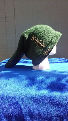 a knitted hat on top of a blue blanket with gold stitchs and an ear hole