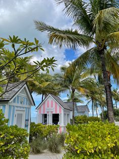 a pink and blue beach hut with palm trees in the foreground on a cloudy day