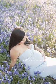 a pregnant woman is sitting in a field of blue flowers and posing for the camera