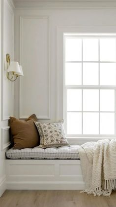 a white window seat with pillows and blankets on it in front of a large window