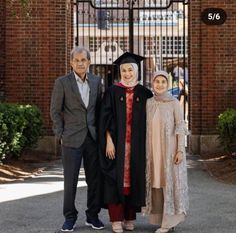 two men and a woman are standing in front of a gate wearing graduation gowns