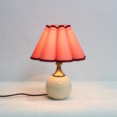 a white lamp with a red shade on it sitting on a table next to a wall