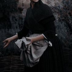 a woman in a black dress and hat with her hands out to the side, posing for a photo