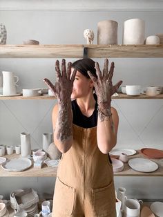 a woman is holding up her hands with mud on them in front of some shelves