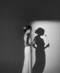 a woman standing in front of a white wall with her shadow on the wall behind her