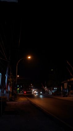 cars driving down the street at night with lights shining in the dark sky behind them