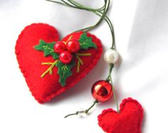 two red heart ornaments with holly and berries hanging from the strings on a white background