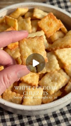 a hand reaching for crackers in a bowl with the words white cheddar on it